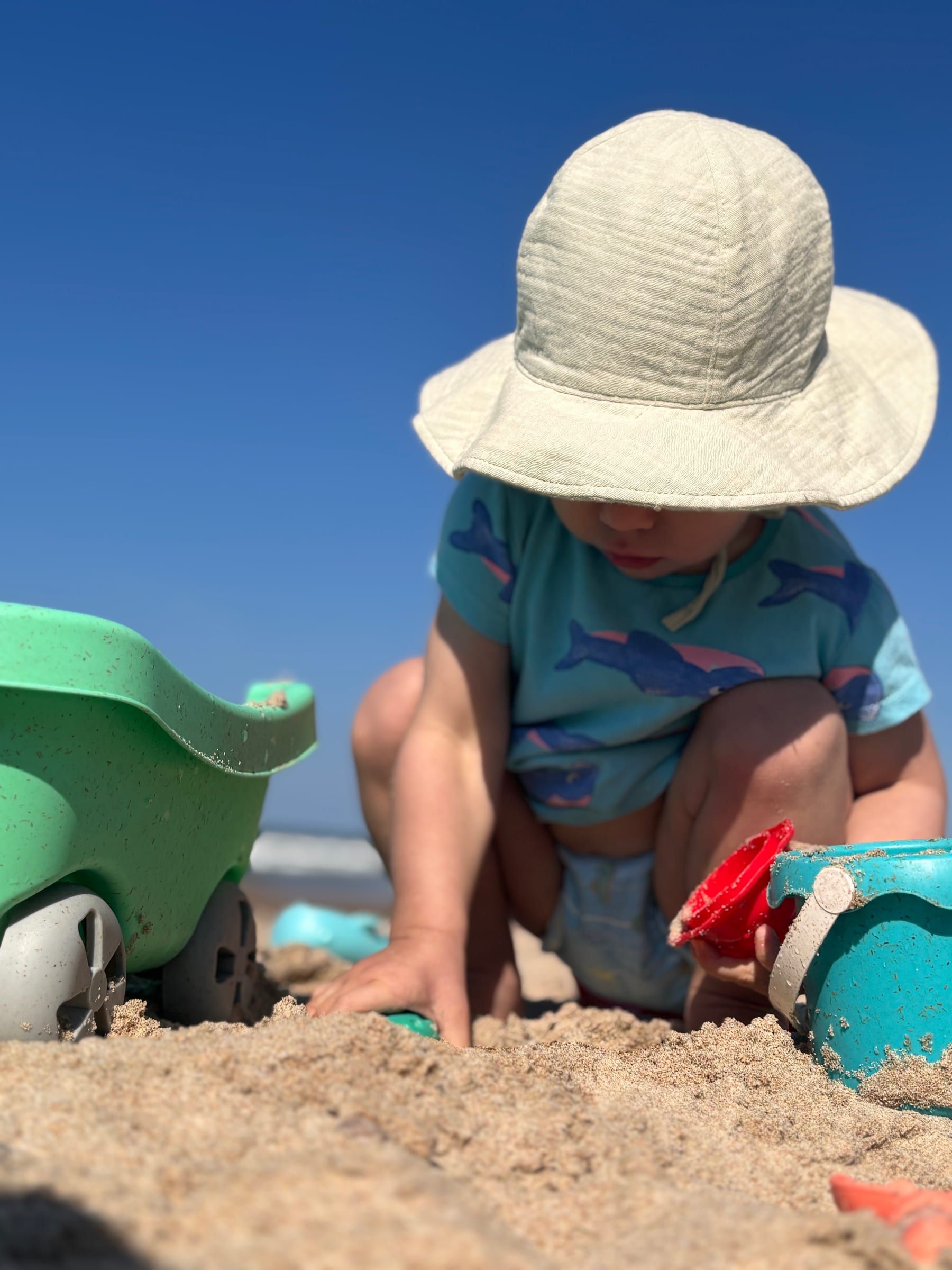 Dziecko w kapeluszu bawi się w piasku na plaży